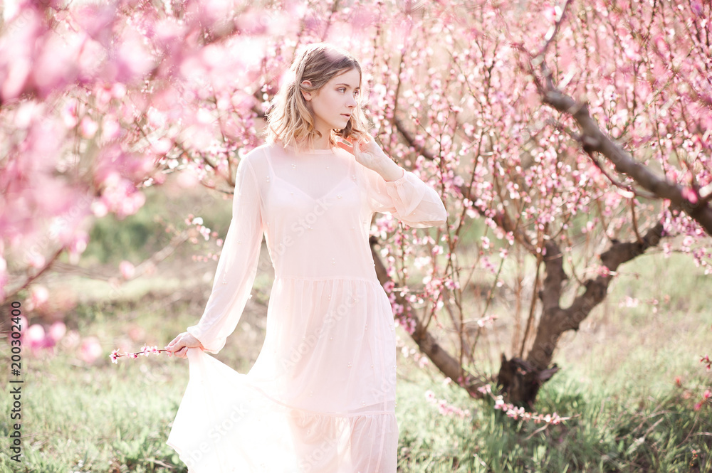 Girl walking in blooming peach orchard. Spring season. 20s. Girl walking in blooming peach orchard. Spring season. 20s.