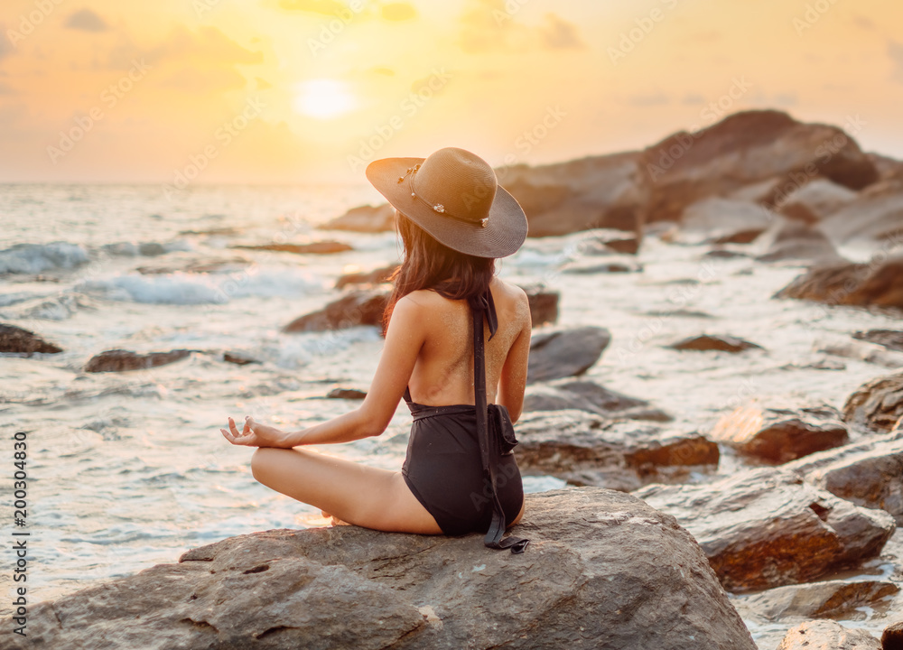 Woman with black swimming suit  practicing yoga meditating on the beach in sunset