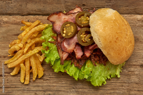 Barbeque Pulled beff Sandwich with green salad,crisp bacon,hot pepper jalapeno,BBQ Sauce and Fries on wooden background,Fast food photo