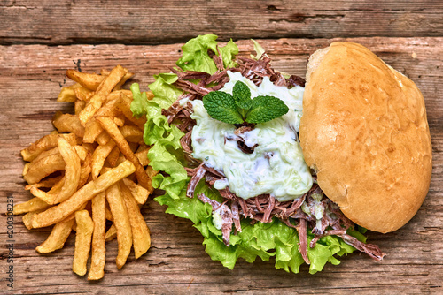 Barbeque Pulled Pork Sandwich with green salad,Tzatziki Sauce,BBQ Sauce and Fries on wooden background