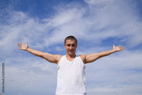 man in a white T-shirt laid his hands wide against the blue sky with clouds.