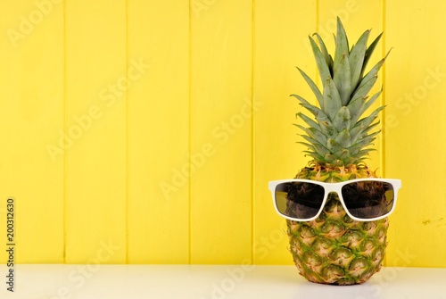 Hipster pineapple with trendy sunglasses against yellow wood background. Minimal summer concept.