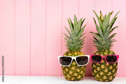 Hipster pineapples with trendy sunglasses against pink wood background. Minimal summer concept.