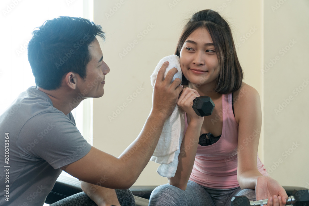 Trainer young handsome man helping wipes sweat off young woman face while resting after workout in fitness gym. Athlete couples, sport exercise concept Trainer young handsome man helping wipes sweat off young woman face while resting after workout in fitness gym. Athlete couples, sport exercise concept