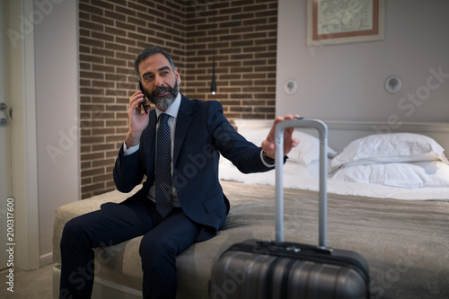 Italian businessman speaking on his smart phone in hotel room and looking through the window. photo