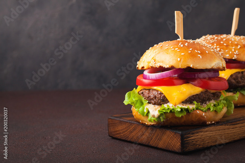 Close-up of delicious fresh home made burger with lettuce, cheese, onion and tomato on a dark background with copy space. fast food and junk food concept