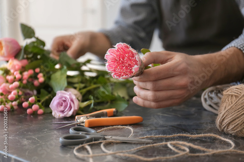 Male florist creating beautiful bouquet at table, closeup photo