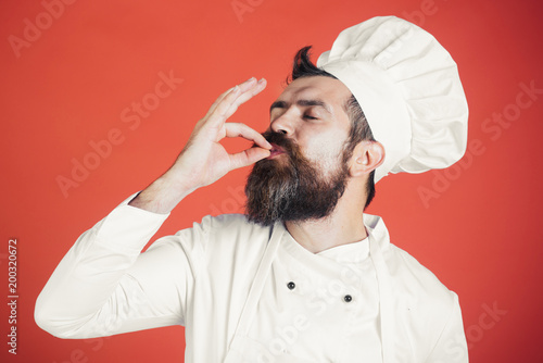 Professional chef man showing sign for delicious. Male chef in white uniform with perfect sign. Serious satisfied bearded chef, cook or baker gesturing excellent. Cook with taste approval gesture. photo