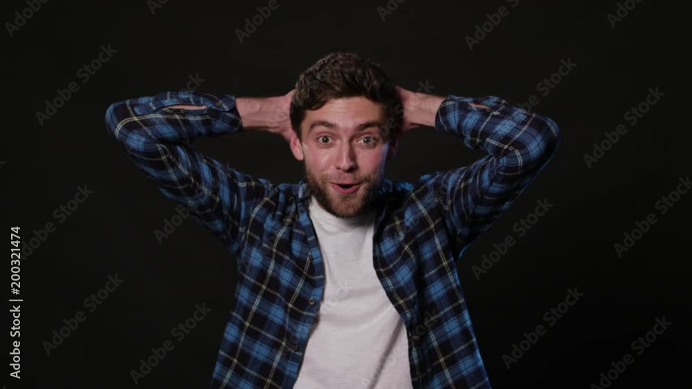 An attractive young man showing delight by touching the back of his head against a black background. Medium Shot An attractive young man showing delight by touching the back of his head against a black background. Medium Shot