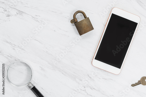 Mobile phone with padlock on top, key and magnifying glass nearby