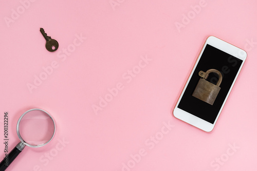 Mobile phone with padlock on top, key and magnifying glass nearby