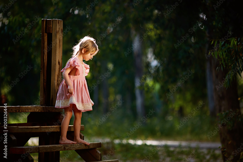 Beautiful little girl in pink dress walking barefoot on the small ...