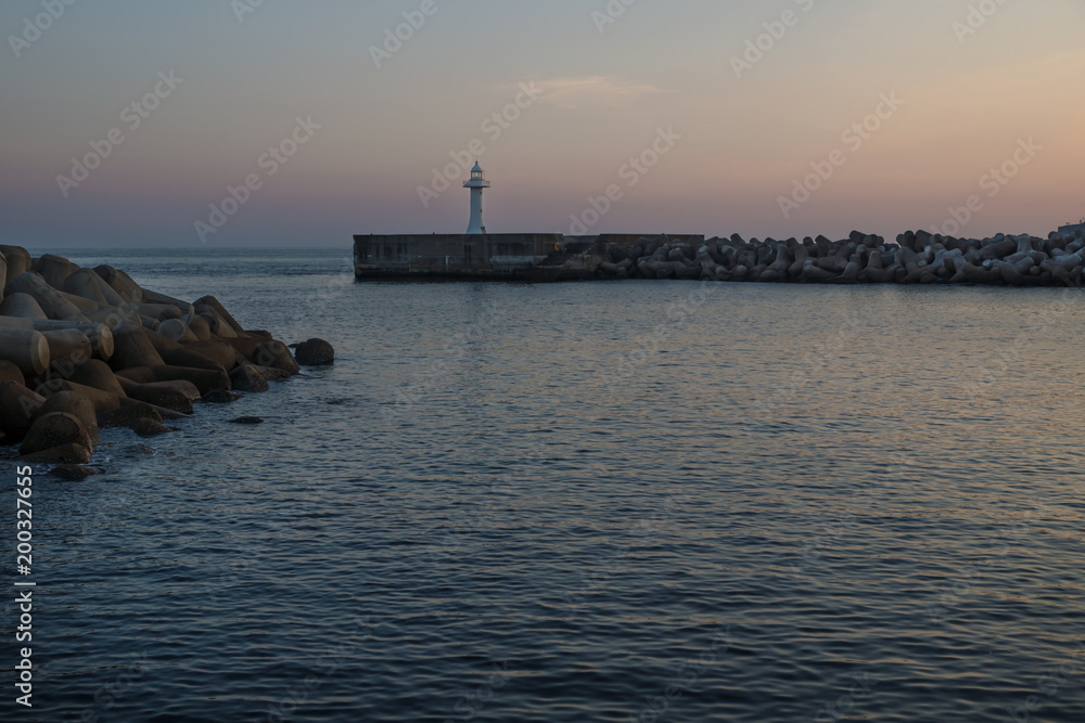 Fototapeta premium White lighthouse with purple light at a seawall with wavebreakers in Seogwipo, Jeju Island, South Korea