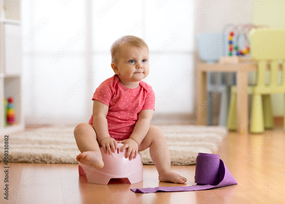 Cute baby girl toddler sitting on chamber pot with toilet paper roll Cute baby girl toddler sitting on chamber pot with toilet paper roll