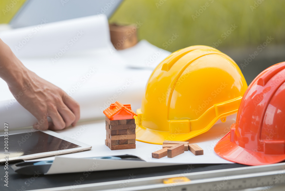 Engineer hard helment with house model and orange roof, working with tablet and computer and white plan Engineer hard helment with house model and orange roof, working with tablet and computer and white plan