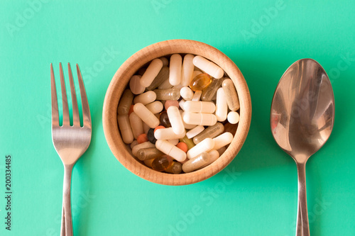 Lots of multicolored pills in a plate on turquoise background . Fork and spoon . The concept of a healthy lifestyle photo