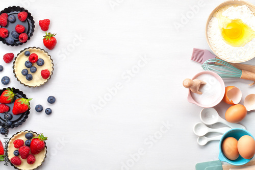 Baking utensils and cooking ingredients for tarts, cookies, dough and pastry. Flat lay with eggs, flour, sugar, berries.Top view, mockup for recipe, culinary classes, cooking blog.
