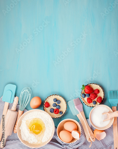 Baking utensils and cooking ingredients for tarts, cookies, dough and pastry. Flat lay with eggs, flour, sugar, berries.Top view, mockup for recipe, culinary classes, cooking blog.