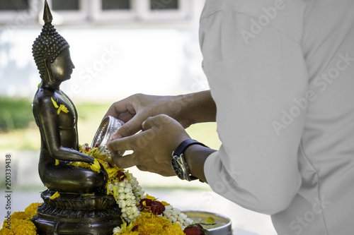 Beautiful Thai cultural. Man pouring water mixed with colourful petal flowers and perfume onto a Buddha image on Songkran festival in Thailand.