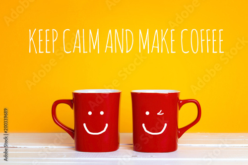 Two red coffee mugs with a smiling faces on a yellow background with the phrase Keep calm and make coffee.