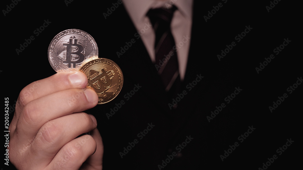 Fototapeta premium A businessman in a suit holds in his hand a gold and silver bitcoin, a black background, a crypto currency, a course.