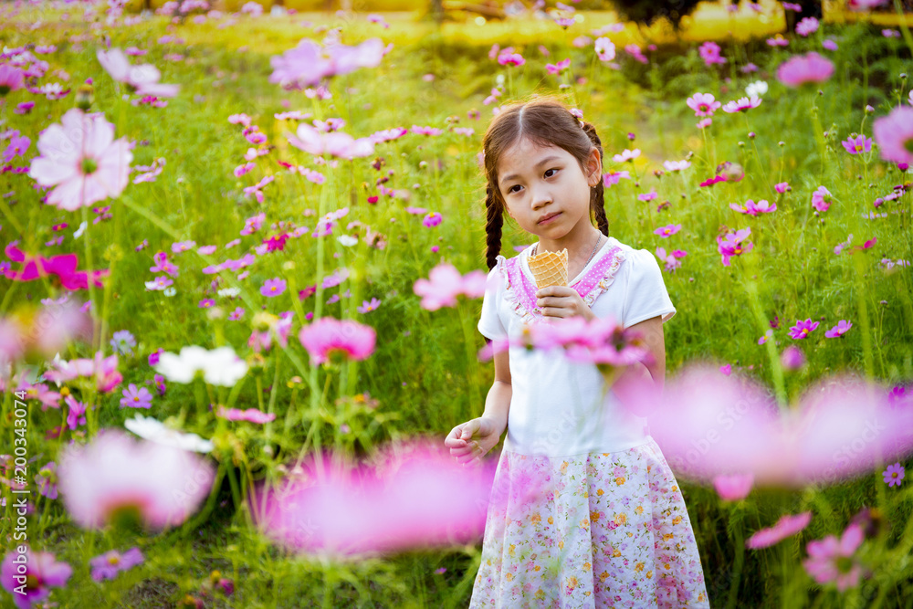 Cute little girl eating ice cream in the field of pink flowers at sunlight Cute little girl eating ice cream in the field of pink flowers at sunlight