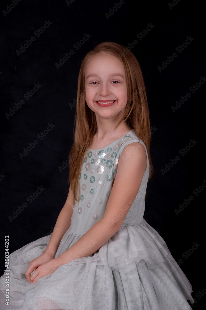 Close up portrait of the smiling of the little girl of the blonde wearing green dress on a dark background in studio. Close up portrait of the smiling of the little girl of the blonde wearing green dress on a dark background in studio.