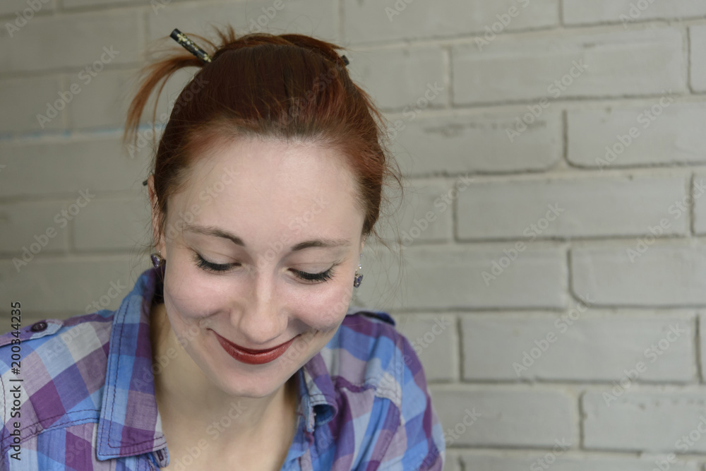 Portrait of red-haired girl in a plaid shirt against a brick wall background Portrait of red-haired girl in a plaid shirt against a brick wall background