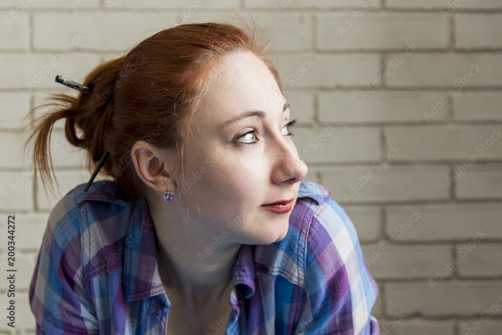 Portrait of red-haired girl in a plaid shirt against a brick wall background Portrait of red-haired girl in a plaid shirt against a brick wall background