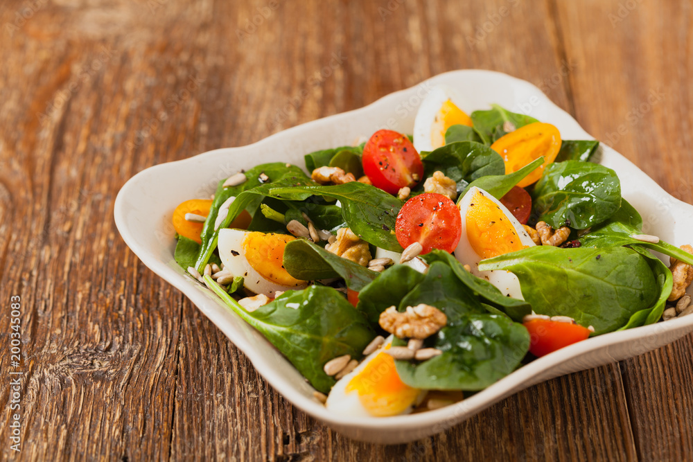 Delicious salad of fresh spinach, boiled egg, tomatoes, nuts and sunflower seeds Delicious salad of fresh spinach, boiled egg, tomatoes, nuts and sunflower seeds