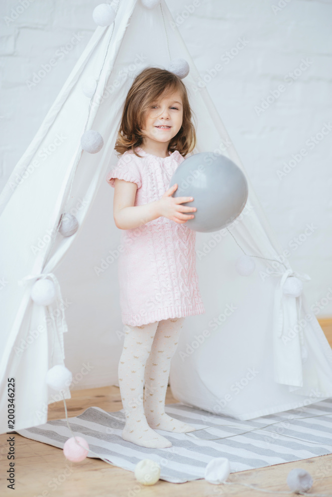 Cute little 3 year old girl standing in pink dress in tent lodge and holding a Cute little 3 year old girl standing in pink dress in tent lodge and holding a