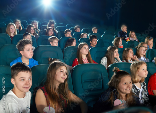 Schoolmates watching fancy cartoon in the cinema. Boys and girls looking happy,emotional, funny and satisfied. Children wearing colorful clothes with prints. Eating popcorn and drinking fizzy drinks. © serhiibobyk