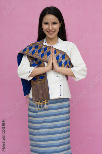 Portrait of asian young girl in traditional thai dress praying isolated on pink background. Wai Sawatdee mean welcome to Thailand. Amazing Travel to Thailand Concept. symbol of Thailand photo