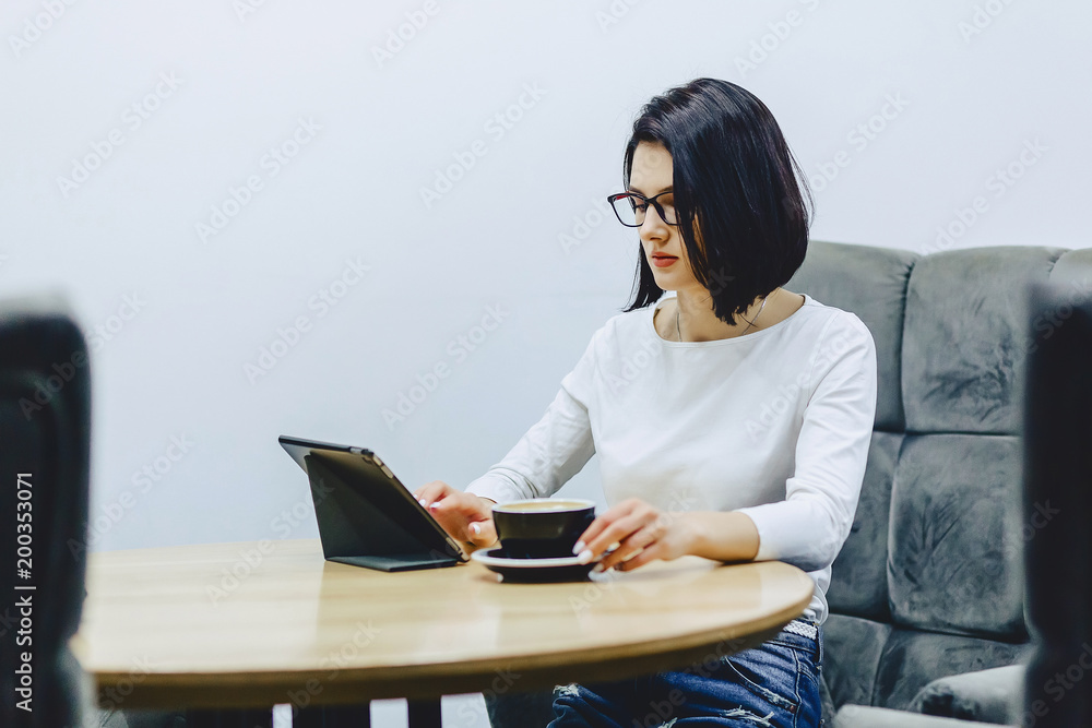 Girl in cafe drinks coffee and works on tablet Girl in cafe drinks coffee and works on tablet