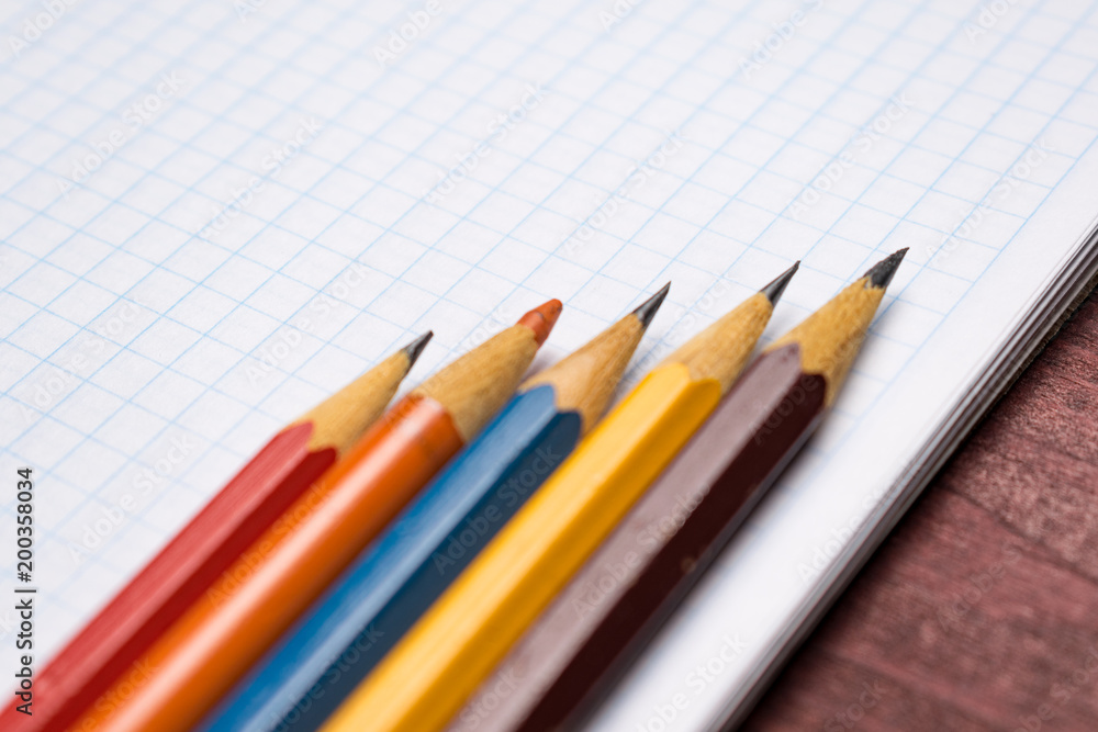 Bright colorful pencils next to a blank sheet of paper. School supplies stationery on a wooden texture table. Trendy minimalism. Concept back to school. Top view Bright colorful pencils next to a blank sheet of paper. School supplies stationery on a wooden texture table. Trendy minimalism. Concept back to school. Top view