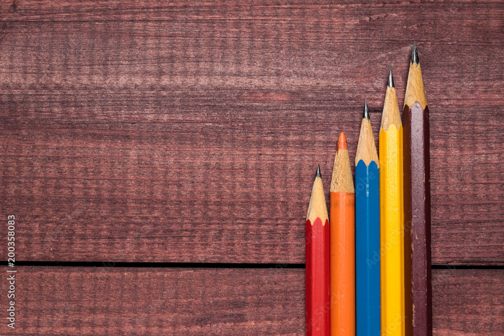 Bright colorful pencils next to a blank sheet of paper. School supplies stationery on a wooden texture table. Trendy minimalism. Concept back to school. Top view Bright colorful pencils next to a blank sheet of paper. School supplies stationery on a wooden texture table. Trendy minimalism. Concept back to school. Top view