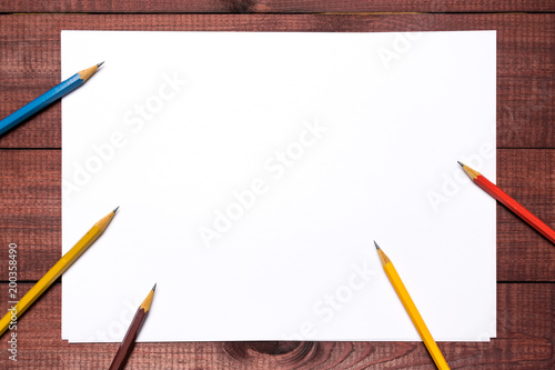 Bright colorful pencils next to a blank sheet of paper. School supplies stationery on a wooden texture table. Trendy minimalism. Concept back to school. Top view