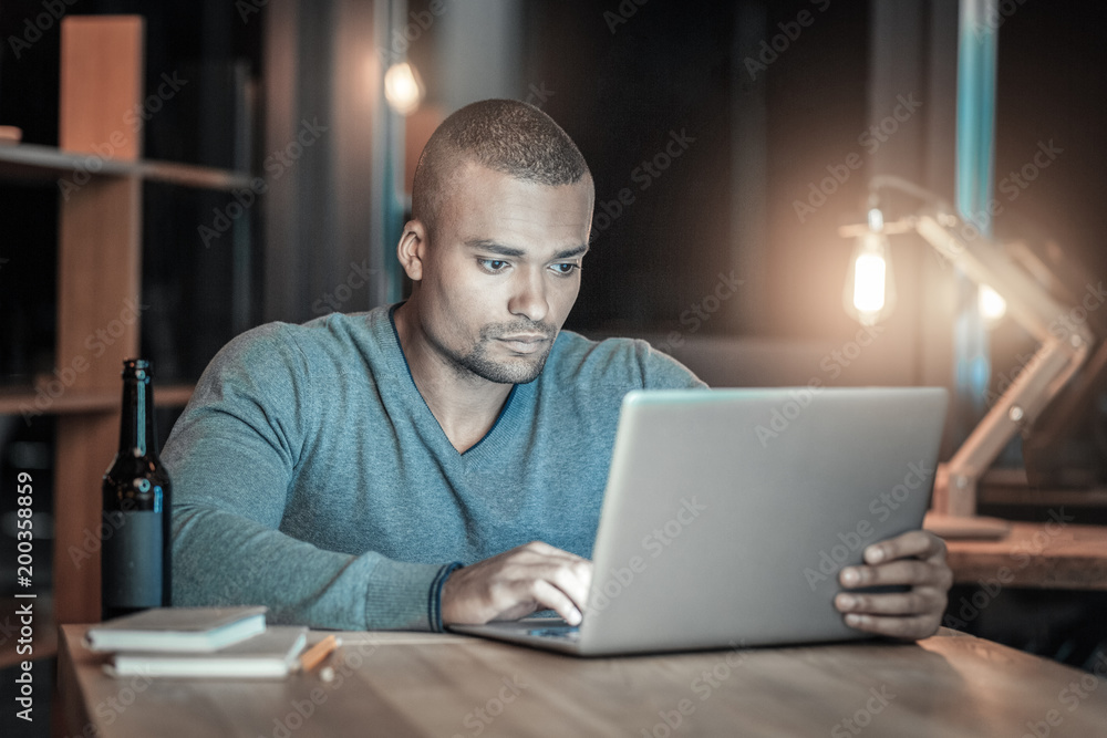 Advanced programming. Attentive concentrated IT guy using laptop while sitting at table and touching laptop Advanced programming. Attentive concentrated IT guy using laptop while sitting at table and touching laptop
