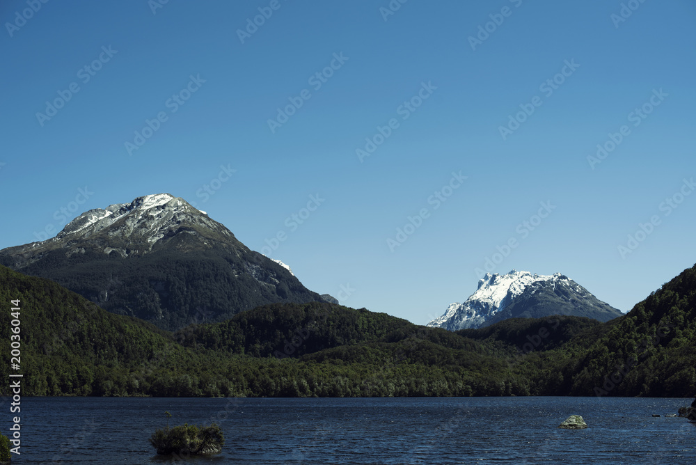 Paisaje de picos de montañas nevados y verdes con cielo azul frente a un lago en Nueva Zelanda Paisaje de picos de montañas nevados y verdes con cielo azul frente a un lago en Nueva Zelanda