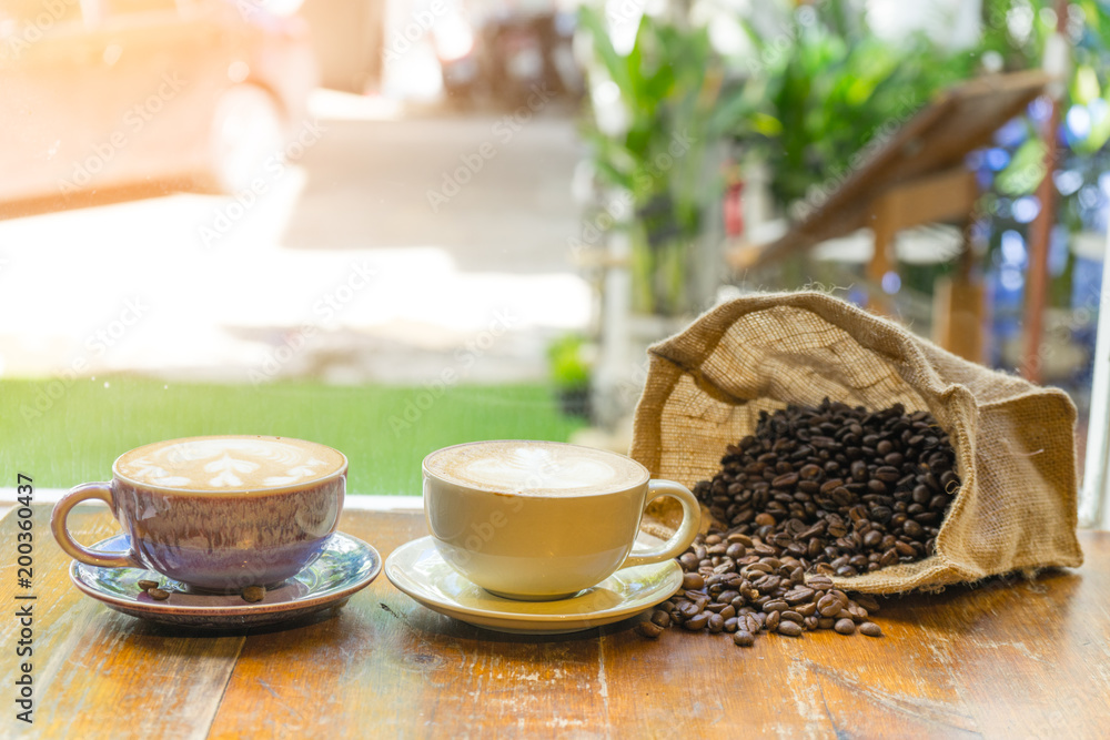 Two cup of latte coffee art with coffee beans in sack on wooden table Two cup of latte coffee art with coffee beans in sack on wooden table