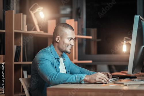 Art of programming. Optimistic handsome IT guy working on computer while posing in profile and smiling