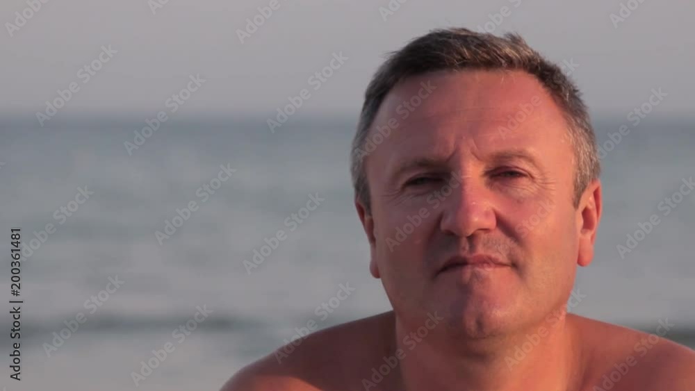 Man on the beach calmly looks in the camera and straightens hair. Man on the background of sea waves. Man on the beach calmly looks in the camera and straightens hair. Man on the background of sea waves.