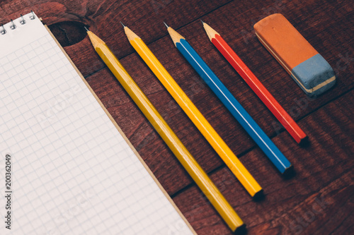 Bright used colorful pencils next to a blank sheet of paper. Work supplies stationery on a wooden texture table. Trendy minimalism. Concept of a modern freelancer workplace. Rustic cozy atmosphere