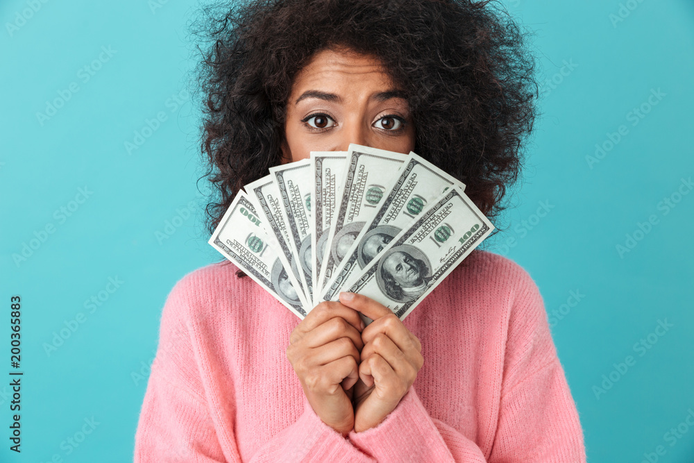 Portrait of excited woman 20s with afro hairstyle covering face with fan of money dollar bills, isolated over blue background Portrait of excited woman 20s with afro hairstyle covering face with fan of money dollar bills, isolated over blue background