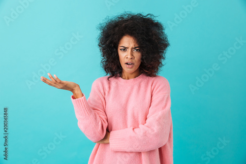 Colorful image closeup of outraged woman with afro hairstyle throwing up hand and expressing misunderstanding, isolated over blue background