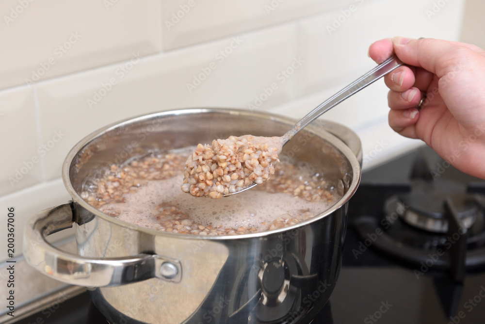 The girl's hand holds cooked buckwheat in a spoon over a saucepan in the kitchen The girl's hand holds cooked buckwheat in a spoon over a saucepan in the kitchen