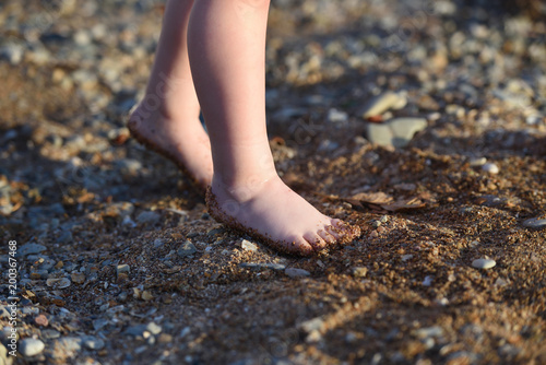 The legs of a small child. The legs of the child go along a sandy beach with pebbles to the sea © pridannikov