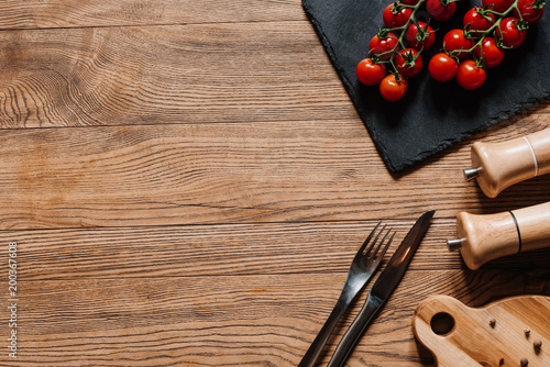 фотографія top view of fresh ripe tomatoes on slate board, fork with knife, seasonings in c