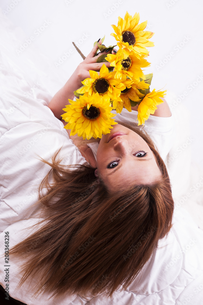 Naklejka premium Beautiful young woman with sunflower lying in bed