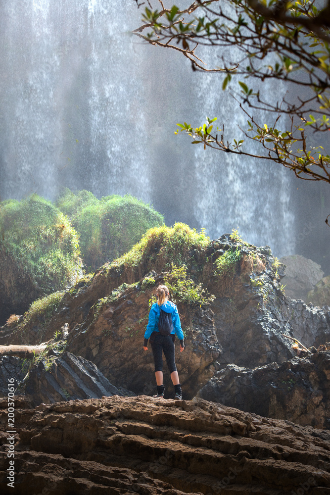 Fototapeta premium Tourist traveler standing on a rock, hiker looking to a Elephant Waterfall below in trip in Vietnam, woman enjoying nature